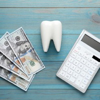 money, a model tooth, and a calculator sitting on a wooden tabletop