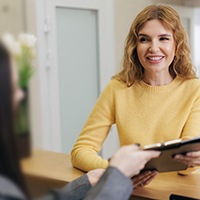 Female patient in yellow sweater smiling at front desk person