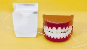 Dental floss container next to a set of toy teeth sitting against a yellow background