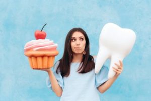 Woman holding a cupcake in one hand and a tooth in the other with a thoughtful look on her face.