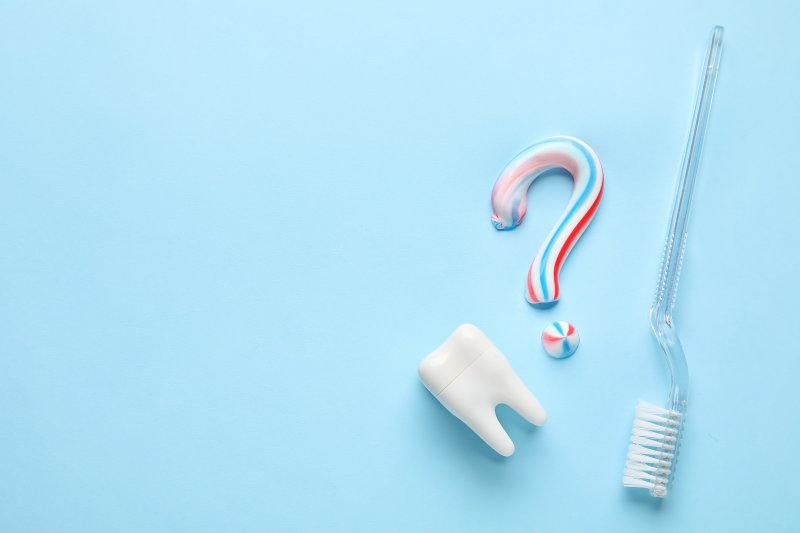 Question mark made of toothpaste, next to fake tooth and toothbrush