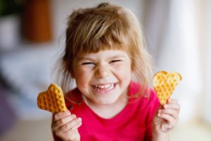 a little girl smiling with heart-shaped waffles in her hands