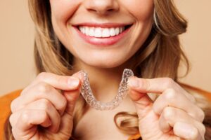 Nose-to-shoulder view of woman in orange shirt holding Invisalign
